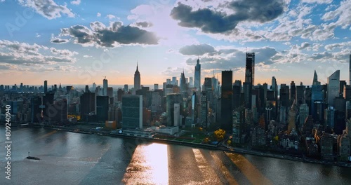 Stunning skyline of New York, USA at sunset. Drone approaches gorgeous buildings at waterfront. Rays of sun hiding behind the clouds light the skyscrapers. photo