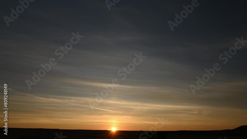 Time lapse of a colorful sunrise with the sun slowly rising above the horizon.  The midground is a flat treeless prairie with small hills.
 photo