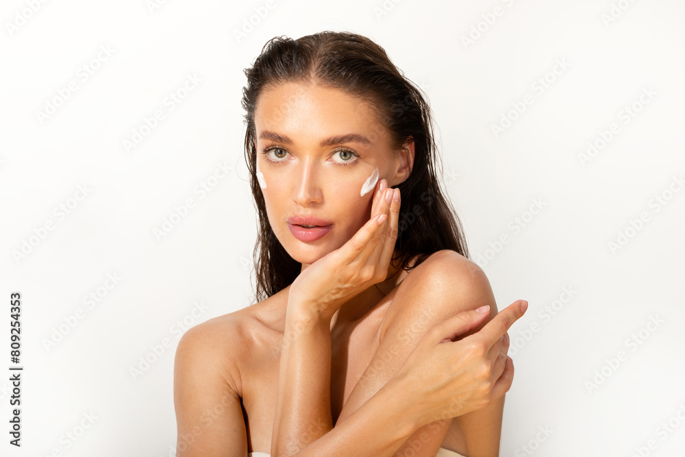 Beautiful woman model looking at camera, caring for herself, enjoying rejuvenation effect of skincare treatment and smooth glowing skin, posing on white background Beautiful woman model looking at camera, caring for herself, enjoying rejuvenation effect of skincare treatment and smooth glowing skin, posing on white background