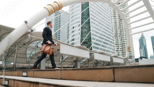 Smart caucasian businessman walking up stairs surrounded by urban view. Side view of ambitious project manager finding challenging job or investment opportunity at city with modern building. Urbane.