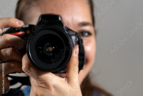 Mujer fotógrafa tomando una fotografía apuntando su cámara al espectador y sonriendo photo