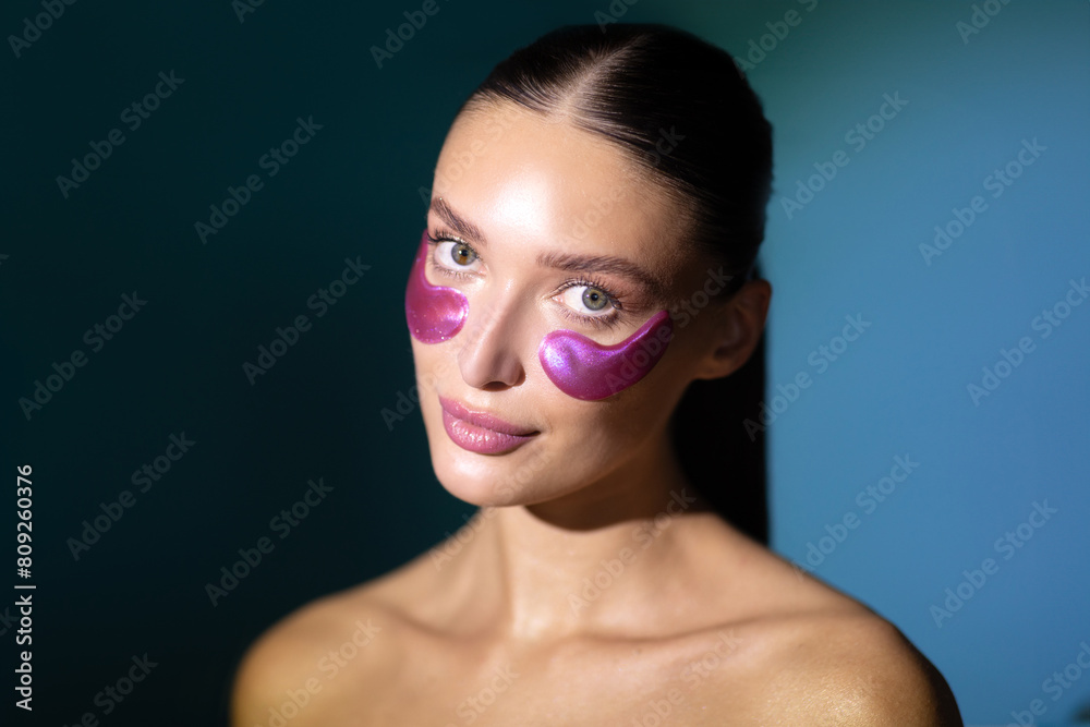 Pretty young woman with under eye patches, enjoy procedures and looking at camera, posing isolated on dark blue background with back light. Skin care, natural beauty, spa treatment Pretty young woman with under eye patches, enjoy procedures and looking at camera, posing isolated on dark blue background with back light. Skin care, natural beauty, spa treatment