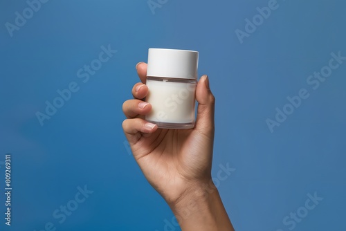Hand holding up cylindrical container with white cap on blue background