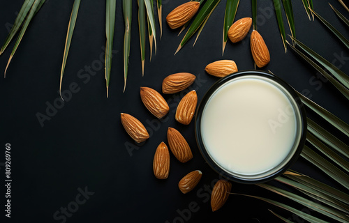 Almond milk in glass and almond nuts with palm leaves on black background