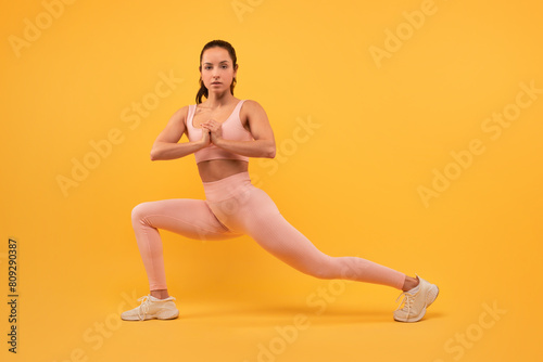 A woman dressed in a pink outfit is focused and balanced as she practices a yoga pose. Her body is aligned, and she displays strength and flexibility in her movement.