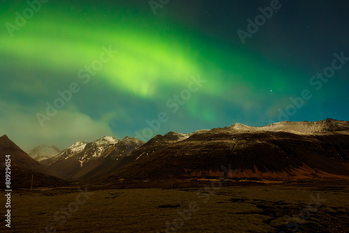 Wintry landscape with aurora borealis above snow covered mountain peaks. Icelandic northern lights magnificent natural phenomenon that brighten up sky  arctic region with magic reflections.