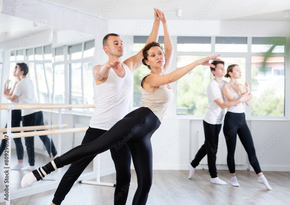 Obraz premium Young active man engaged in dance hall with female partner and practicing ballet arabesque pose during group class. Hobby, healthy lifestyle concept