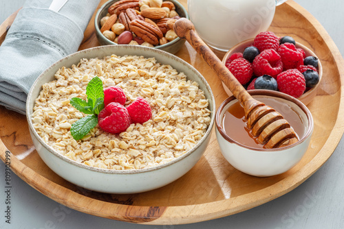 Bowl of porridge or oatmeal with different ingredients on wooden tray. Breakfast serving. photo