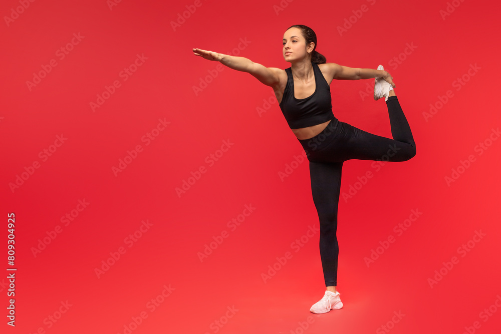 Obraz premium A woman dressed in a black top and leggings is demonstrating a yoga pose. She is focused and balanced, holding a steady position with precision and control