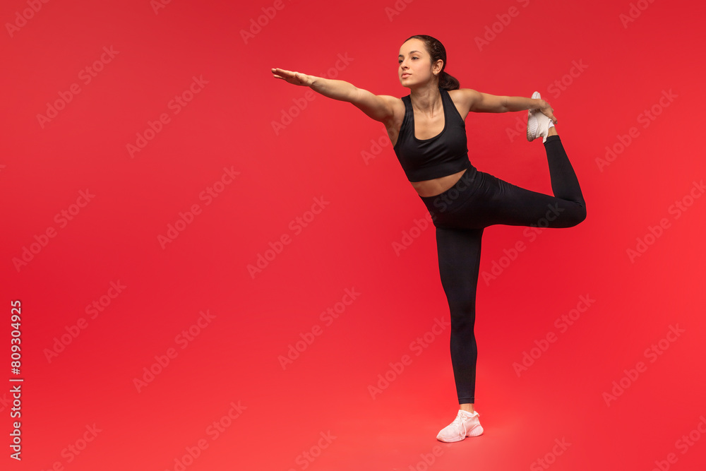 A woman dressed in a black top and leggings is demonstrating a yoga pose. She is focused and balanced, holding a steady position with precision and control
