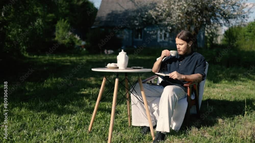 male writer-landowner drinks coffee from a service on a table in the garden in the spring and reads a book at home. male writer-landowner drinks coffee from a service on a table in the garden in the spring and reads a book at home.