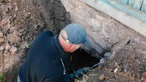 male worker drills the foundation with a hammer drill for sewerage in a country house.