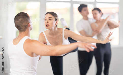 Portrait of positive young man and female partner training ballet pose with group of guys and girls in modern dance class
