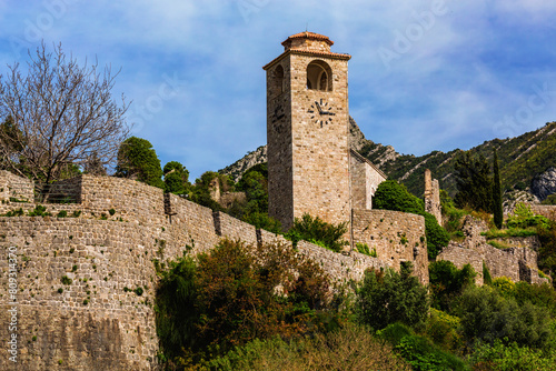 Old Bar, Montenegro. Striking view of the ancient clock tower and stone walls, vivid greenery and clear blue skies, historical and travel themes © Elena