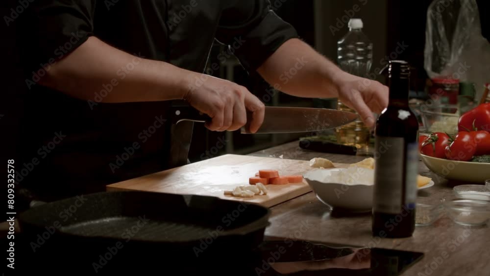 Male chef is chopping potatoes with precision on an aesthetically pleasing cutting board. There is a bottle of red wine nearby, and various vegetables for cooking are scattered around. Medium shot Male chef is chopping potatoes with precision on an aesthetically pleasing cutting board. There is a bottle of red wine nearby, and various vegetables for cooking are scattered around. Medium shot