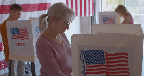 A group of diverse and focused voters voting at a polling station with sliding glass doors, American flags and trees in the background