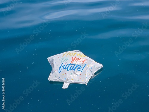 Deflated star-shaped graduation balloon floating on calm blue Lake Michigan water