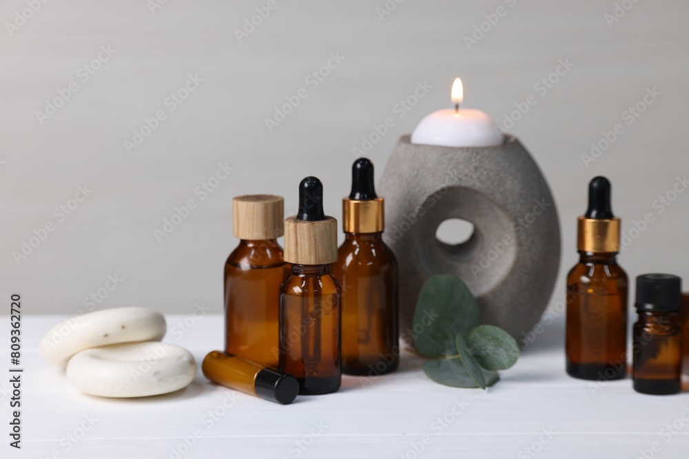 Different aromatherapy products, burning candle and eucalyptus leaves on white wooden table Different aromatherapy products, burning candle and eucalyptus leaves on white wooden table