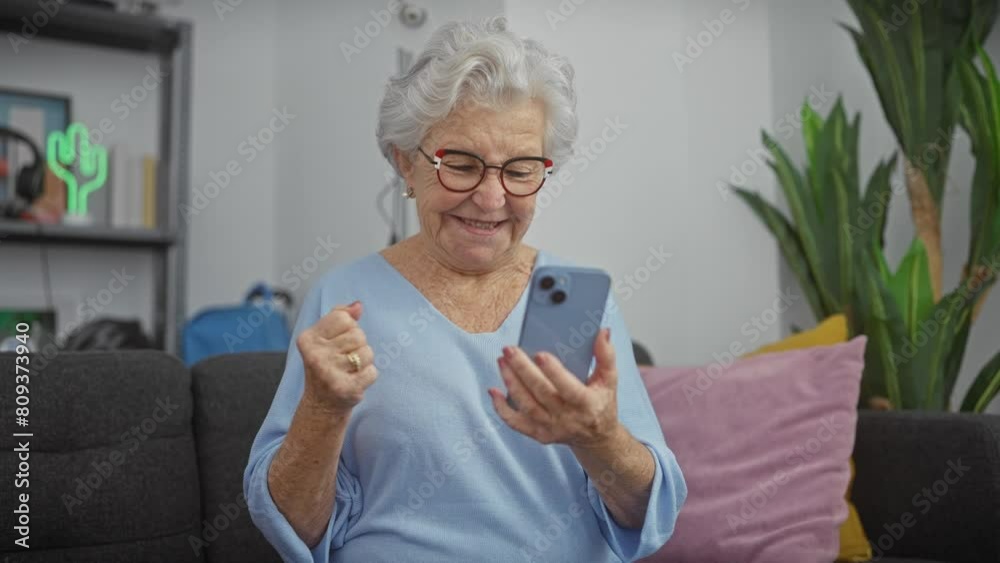 Elderly woman using smartphone with excitement in a cozy living room Elderly woman using smartphone with excitement in a cozy living room