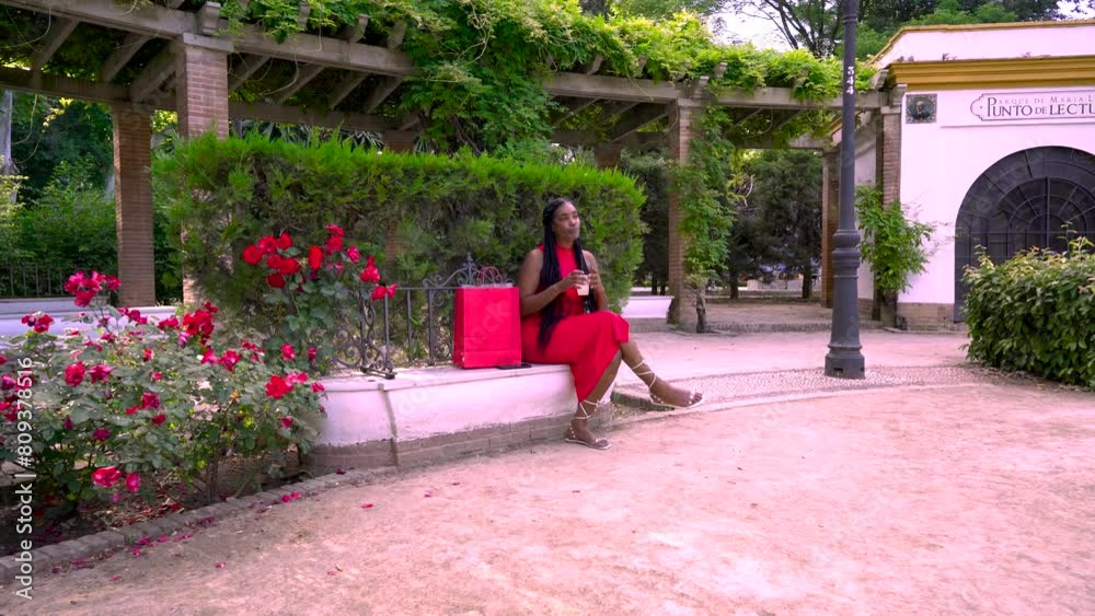 Mujer alegre sentada en un parque con una bebida refrescante revisando las compras que ha hecho en las tiendas y llamando a su amiga por el teléfono móvil.