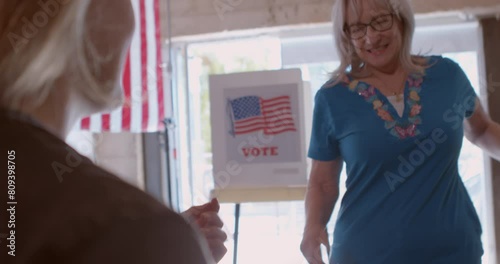 A young female poll worker processing voters at a polling station draped with American flags. 