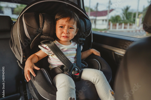 crying toddler girl sitting in car seat, safety baby chair travelling