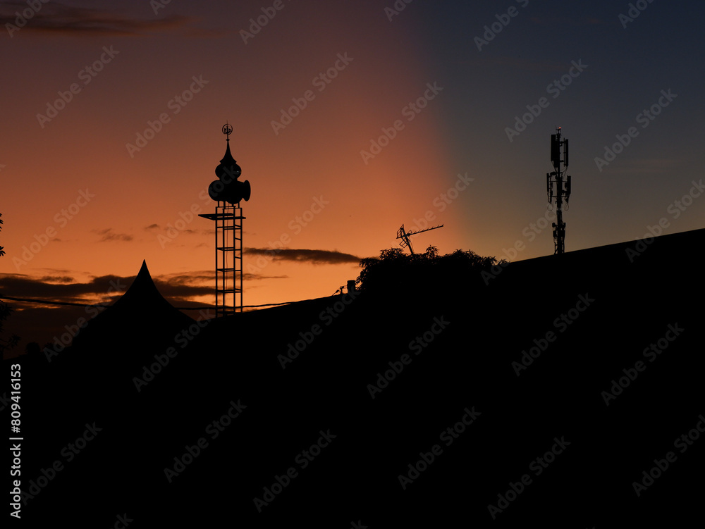 Obraz premium The silhouette of a mosque tower against the sunrise and blue sky