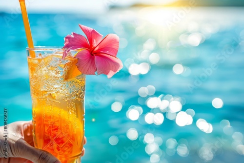 A close-up of a cocktail with a tropical garnish, held by someone enjoying a summer boat cruise, with the turquoise ocean 