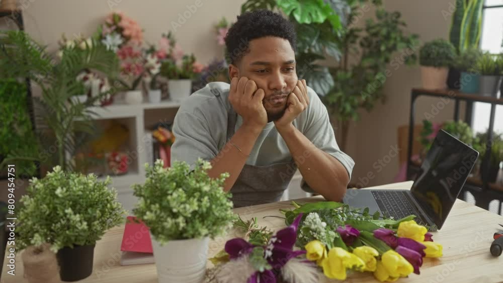 Thoughtful african man in flower shop with laptop surrounded by assorted blooms creating a serene environment. Thoughtful african man in flower shop with laptop surrounded by assorted blooms creating a serene environment.