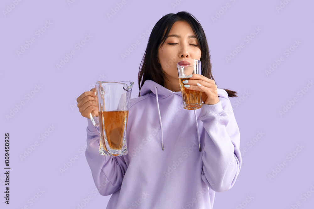 Beautiful Asian woman drinking juice on lilac background Beautiful Asian woman drinking juice on lilac background