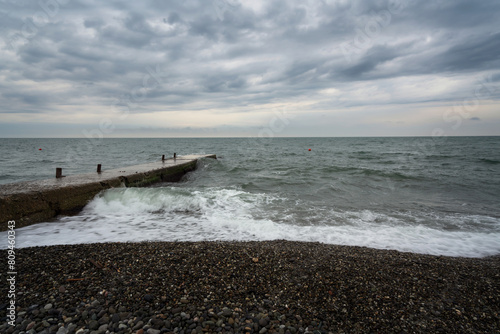 Stormy Black Sea on the Sochi coast and a concrete breakwater on a city beach on a summer day with clouds, Sochi, Krasnodar Territory, Russia photo