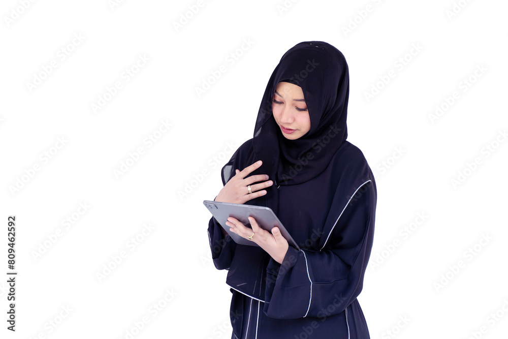 Muslim student wearing Abaya niqab traditional clothes standing review the lesson on tablet for the exam in university on white wall background. Muslim student wearing Abaya niqab traditional clothes standing review the lesson on tablet for the exam in university on white wall background.