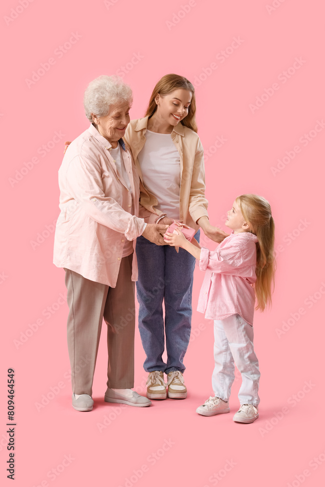 Little girl giving her mother and great-grandma gift on pink background Little girl giving her mother and great-grandma gift on pink background