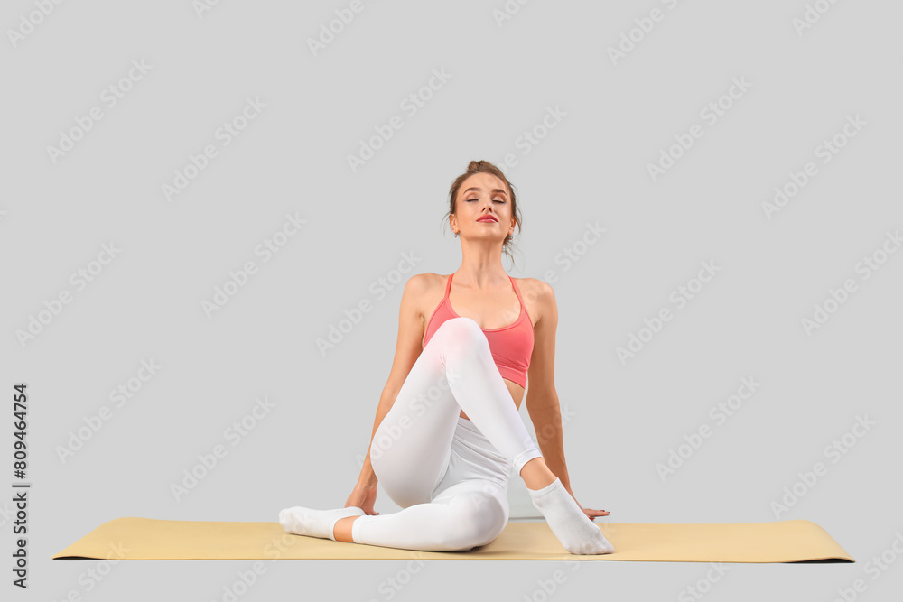 Fototapeta premium Young woman doing yoga on grey background