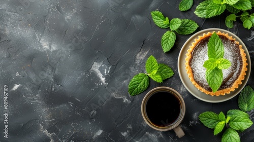   A dessert on a plate, a cup of coffee nearby, and fresh mint leaves atop a black stone table - an overhead perspective photo