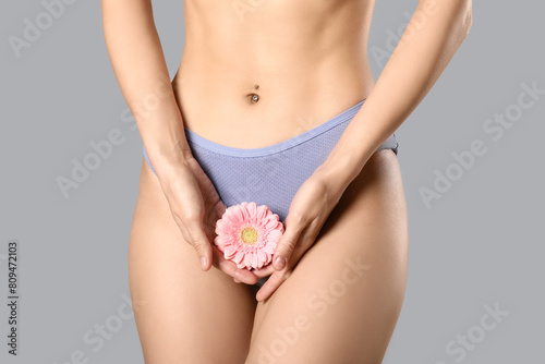 Young woman in panties with beautiful pink flower on grey background