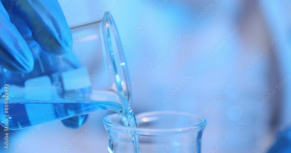 Scientist in latex gloves pours liquid into glass beaker Scientist in latex gloves pours liquid into glass beaker