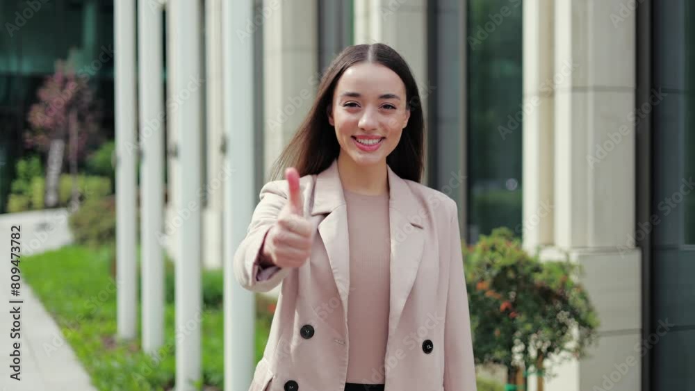 Excited female trainee making like sign and smiling to camera with proud look on background with office exterior. Enthusiastic junior programmer getting ready for first working day in company. Excited female trainee making like sign and smiling to camera with proud look on background with office exterior. Enthusiastic junior programmer getting ready for first working day in company.