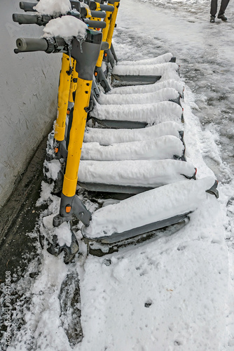 Parked electric scooters are covered with snow on a spring day