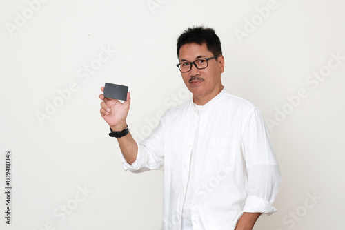Adult Asian guy standing in his casual clothes, showing his business card he is holding with his right hand photo