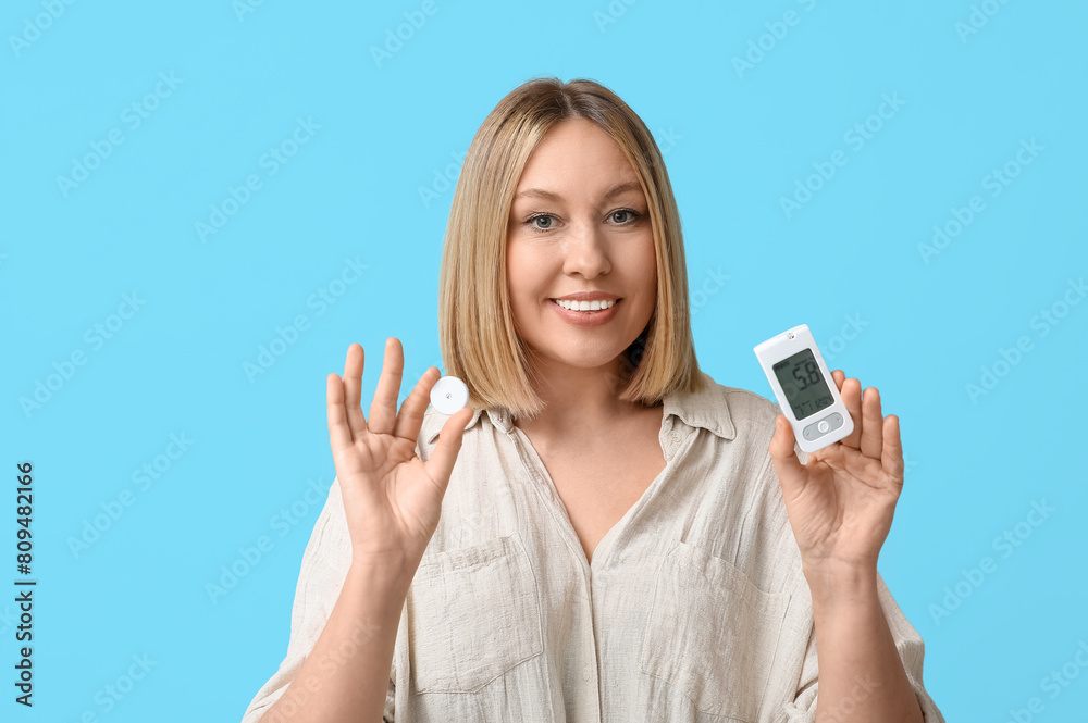Woman with glucometer and sensor for measuring blood sugar level on blue background. Diabetes concept