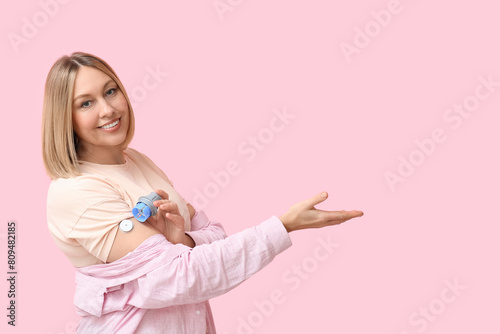 Woman with glucose sensor for measuring blood sugar level and applicator showing something on pink background. Diabetes concept