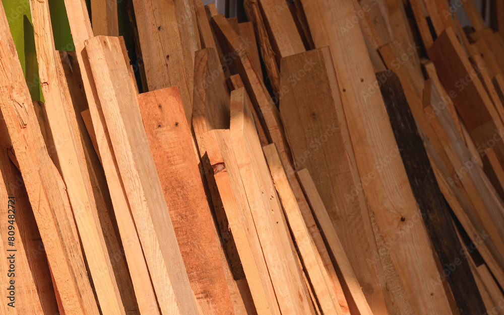 Row of many old timbers leaning against the wall in storage room with light and shadow on surface, remaining wooden material used for reuse and recycling concept