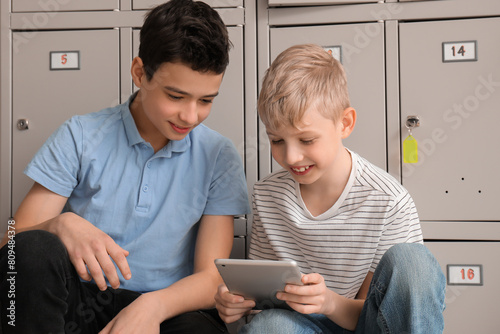 Little schoolboys using tablet computer near locker at school photo