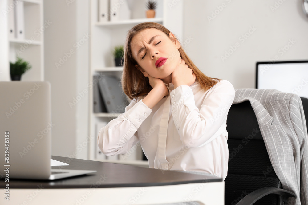 Young businesswoman suffering from neck pain at table in office Young businesswoman suffering from neck pain at table in office