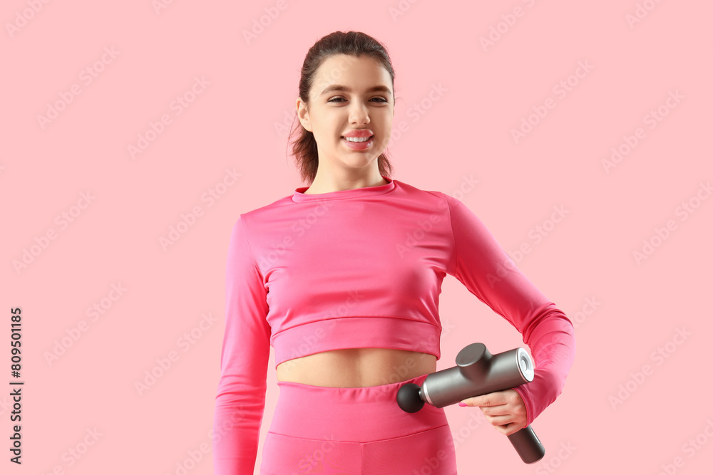 Sporty young woman massaging her belly with percussive massager on pink background Sporty young woman massaging her belly with percussive massager on pink background