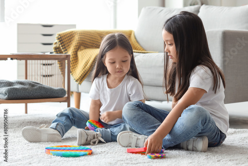 Cute little Asian happy sisters playing with different pop it fidget toys on floor at home