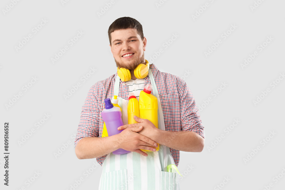 Young bearded man with bottles of detergent on light background Young bearded man with bottles of detergent on light background