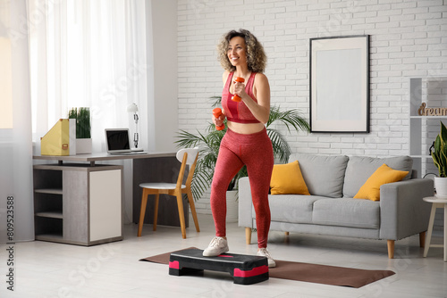 Fotografie Happy mature sporty woman training with stepper and dumbbells at home