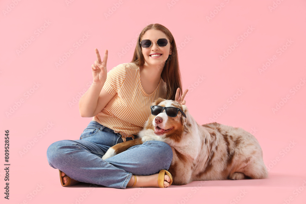 Young woman and cute Australian Shepherd dog with sunglasses showing victory gestures on pink background Young woman and cute Australian Shepherd dog with sunglasses showing victory gestures on pink background